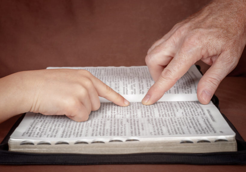 Hand of man pointing something to a child in the Bible book. Teaching a disciple from the Bible.